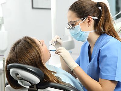 A dental professional in a blue gown assisting a patient with dental care, set in a modern dental office.