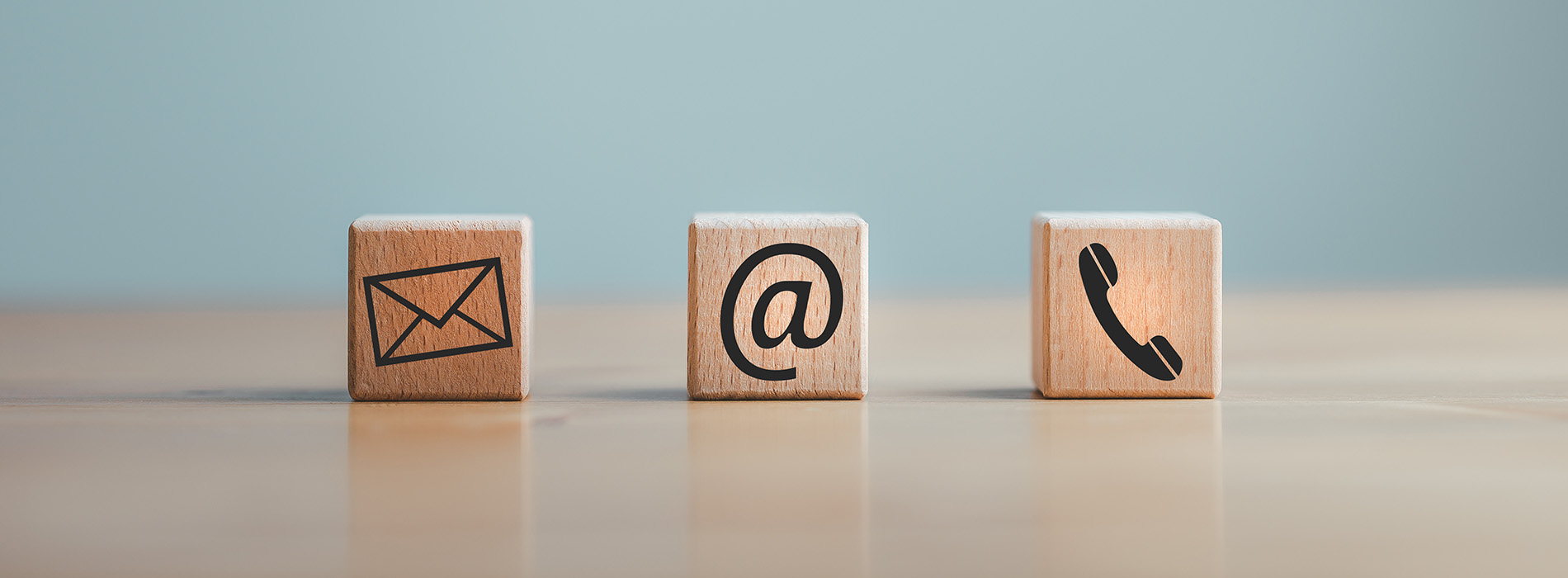 The image shows four wooden blocks with symbols representing communication methods  an envelope for mail, a phone for voice calls, a computer icon for digital communication, and a smartphone symbol for mobile devices, arranged on a flat surface against a blue background.