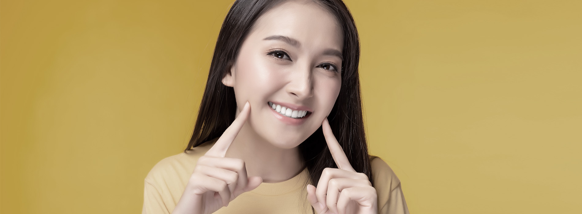 A woman with long hair smiles at the camera while holding up her hand with fingers spread apart.