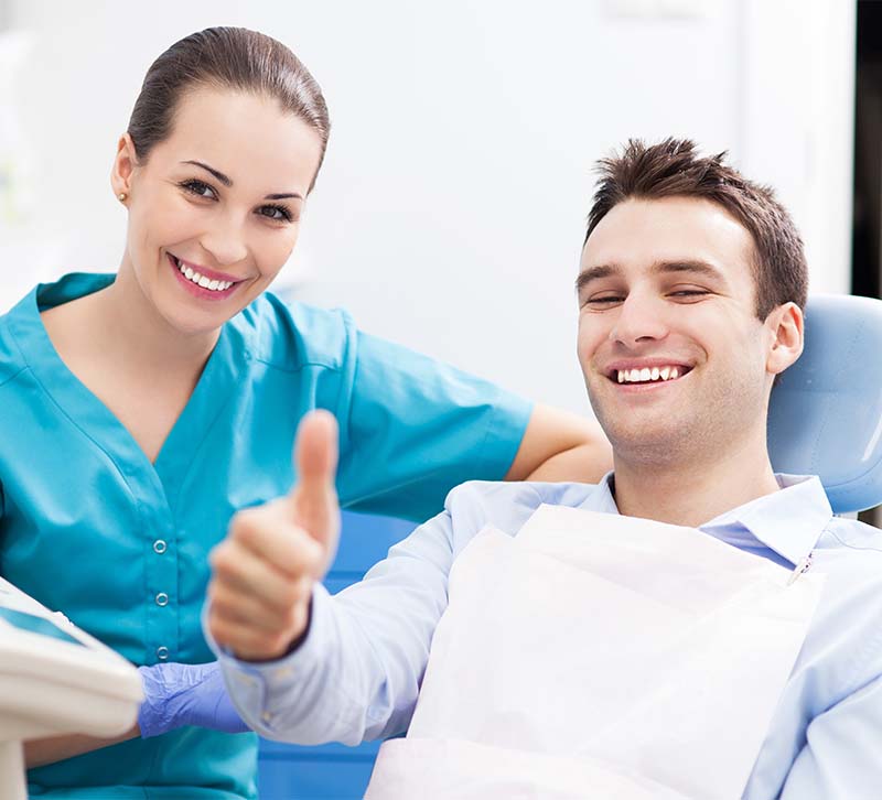 The image features a smiling man in a dental chair, with a woman standing behind him, both in a dental office setting, suggesting a positive dental care experience.