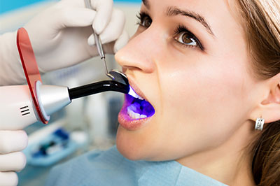 The image shows a person sitting in a dental chair with a dentist s hand holding a device over their mouth, likely for a dental procedure.