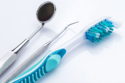 The image shows a collection of dental tools including a toothbrush with blue bristles, a pair of tweezers, a metal loop, and other dental instruments on a white surface.