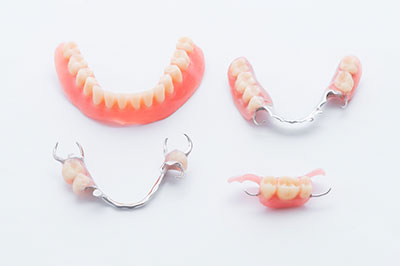 The image displays three pairs of dentures with teeth showing, each pair placed on a separate surface with a clear background.