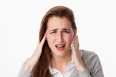 The image features a woman with her hand on her head, appearing to be experiencing discomfort or pain, possibly due to stress or headache, set against a plain background.