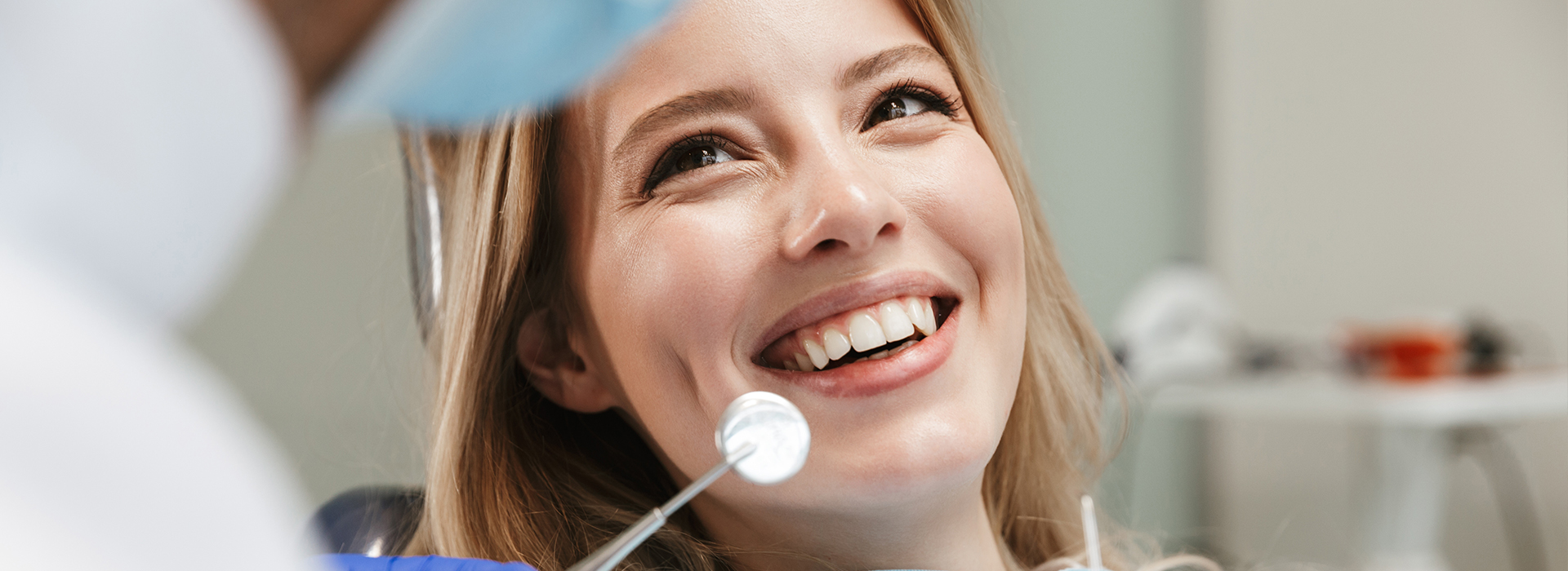 Woman sitting in dental chair with smiling expression, looking towards camera.