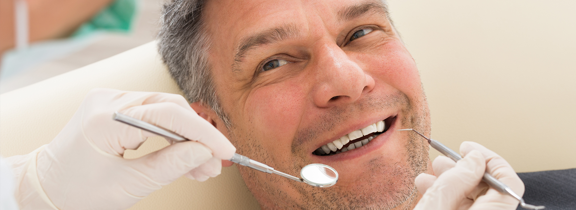 The image shows a man sitting in a dental chair with his mouth open, receiving dental care from a professional wearing gloves and using dental instruments.