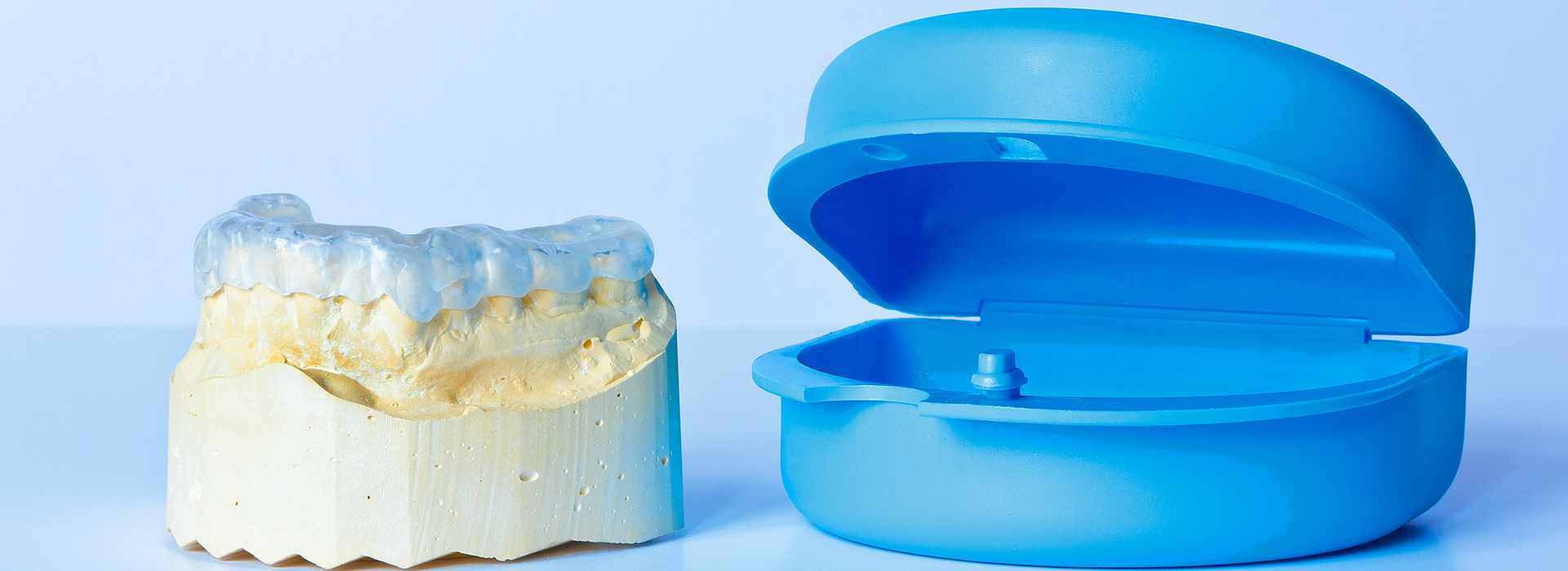 The image shows a clear plastic dental implant on the left side and a blue plastic model of a dental implant with a screw visible on the right, both set against a white background.