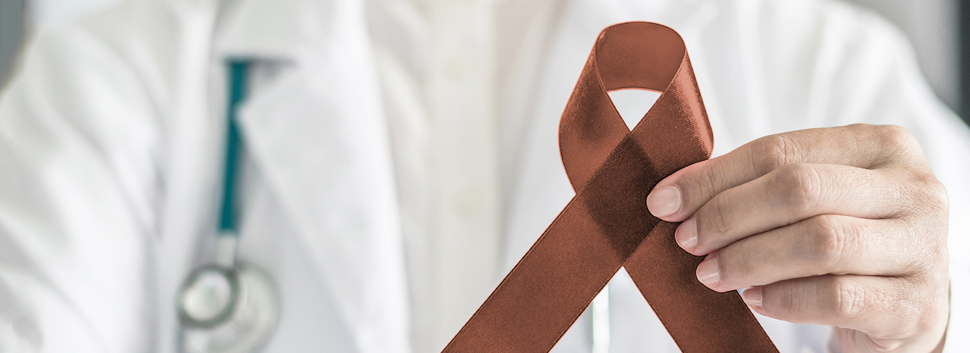 The image features a healthcare professional holding an orange ribbon with a brown bow, symbolizing awareness for cancer.