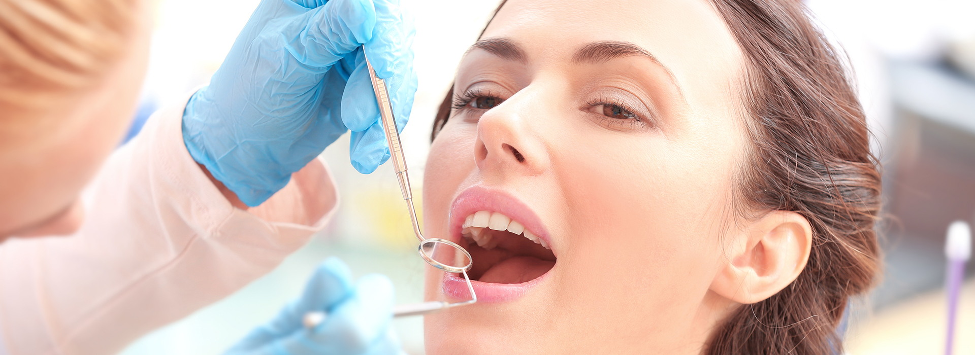 The image depicts a woman receiving dental care with a focus on her open mouth and the dental instruments being used.