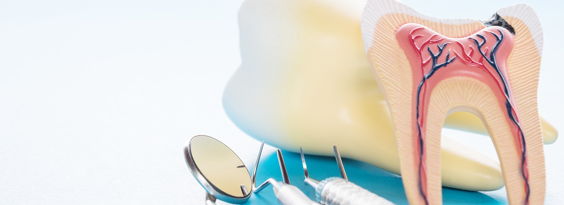 The image shows a close-up of dental tools with a tooth model in the foreground, placed against a blue background, possibly for educational or promotional purposes.