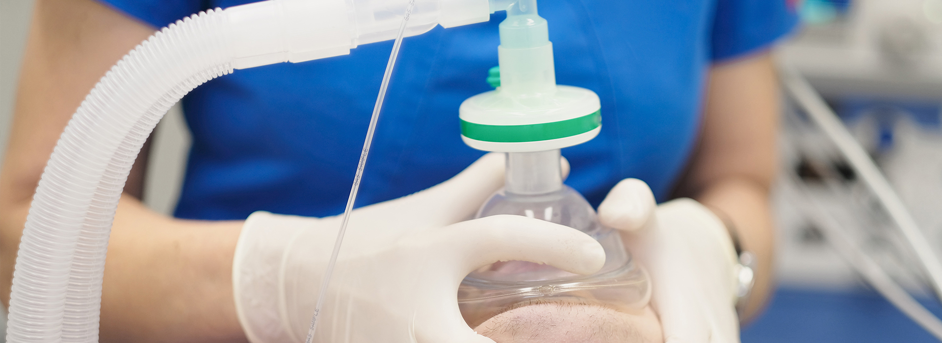 A person wearing gloves is handling a medical device with a transparent tube connected to it.