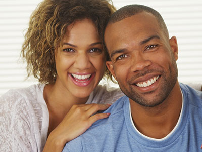 A man and woman are smiling at the camera, with the man wearing a blue t-shirt and the woman in a white blouse  they appear to be in a happy, intimate moment, possibly celebrating an occasion or enjoying each other s company.