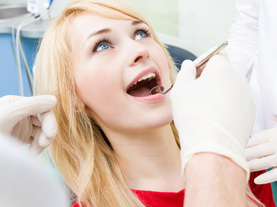 A woman sitting in a dentist s chair with her mouth open, receiving dental care from a professional holding tools.