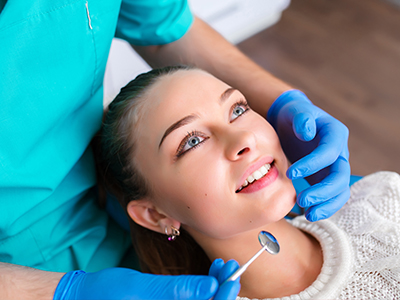 A dental hygienist performing a teeth cleaning procedure on a woman s mouth, with the woman sitting in a dental chair and holding her chin.