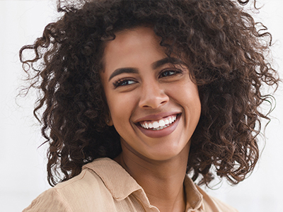 The image features a smiling woman with curly hair, wearing a light-colored top, set against a plain background.